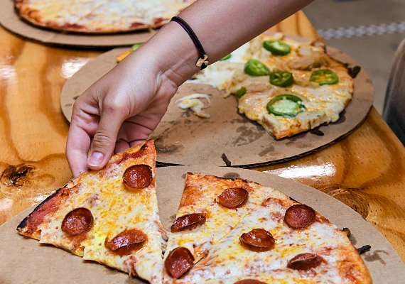 A woman's hand picking up a pepperoni pizza slice.